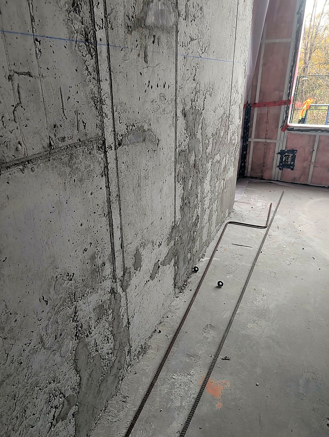 Concrete wall with surface defects and patching in progress, rebar staged on the floor