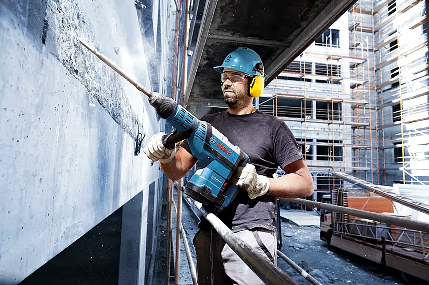 Worker chipping a concrete wall with a rotary hammer on a high-rise site